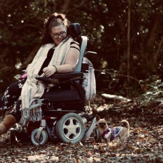 A photo of Active8 member, Heather, in her electric wheelchair, walking her dog in the woods.
