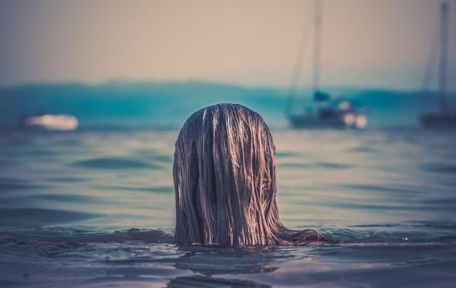 A woman swimming in the sea with boats in the background.